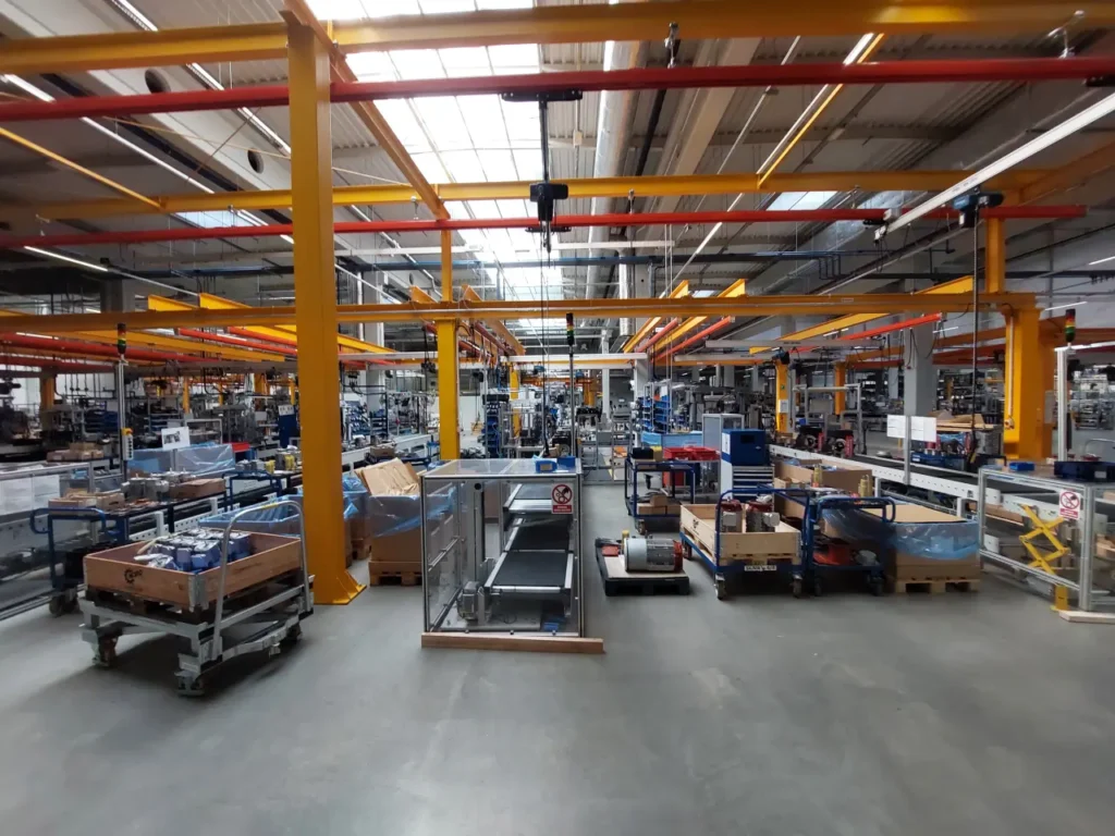 Czerwone suwnice modułowe z wciągnikami łańcuchowymi na torach jezdnych w hali montażowej