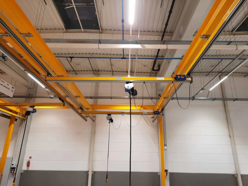 Suwnice modułowe z wciągnikami łańcuchowymi na żółtej konstrukcji wsporczej w hali montażowej