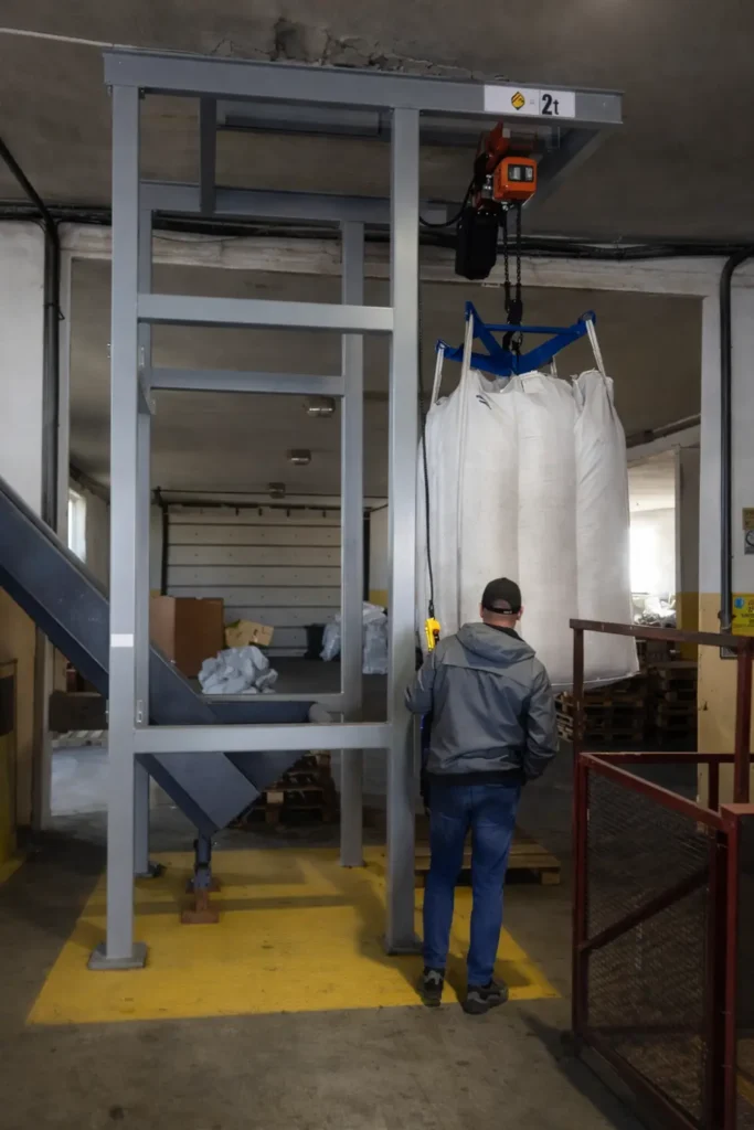 Worek BIG-BAG uniesiony wciągarką nad stanowiskiem opróżniania materiałów sypkich