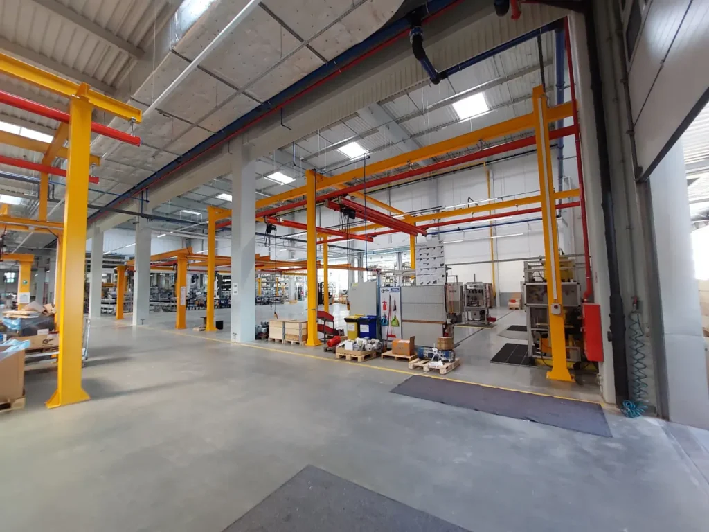 Czerwona suwnica modułowa z wciągnikiem łańcuchowym na konstrukcji wsporczej w hali serwisowej